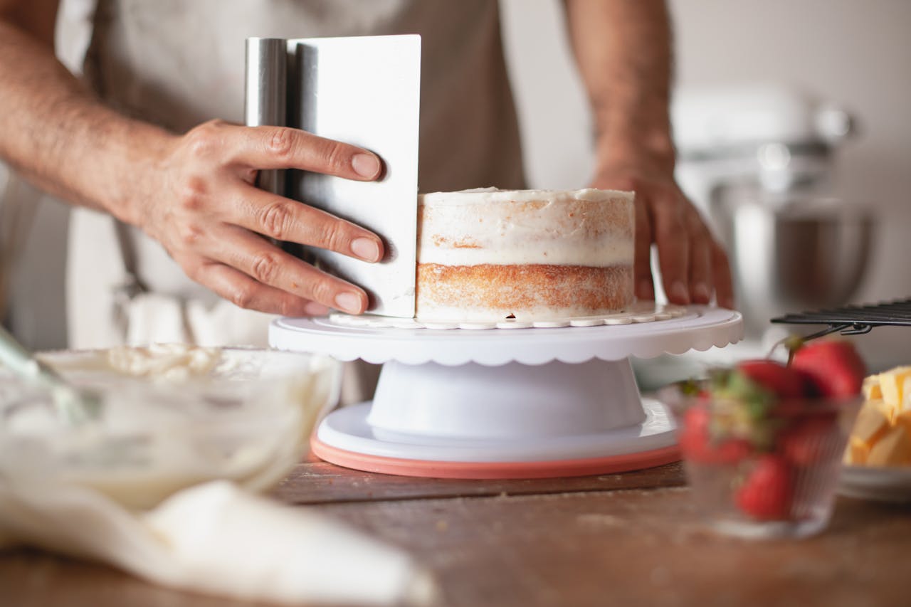 Close-up of a baker applying frosting on a fresh cake indoors.